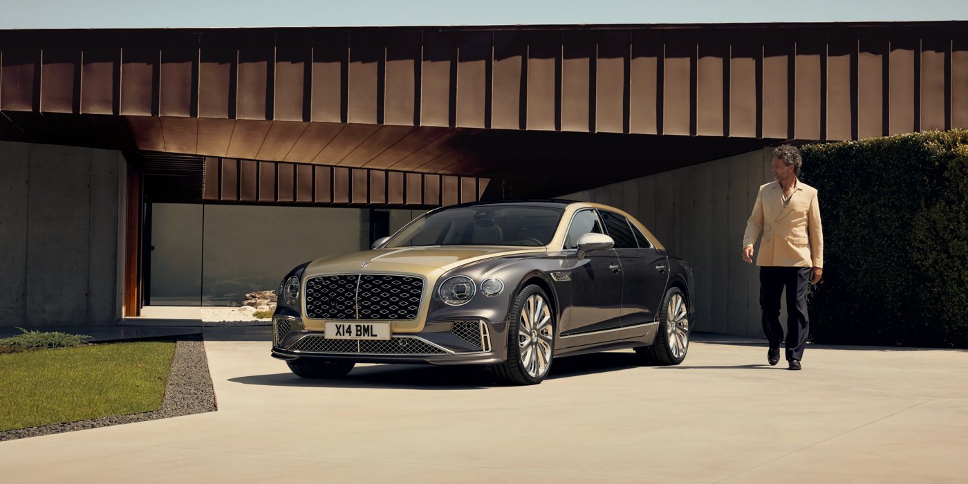 Bentley Hampshire Bentley New Flying Spur Mulliner V8 hybrid sedan front three quarters in Rose Gold over Magnetic paint, parked near modern home