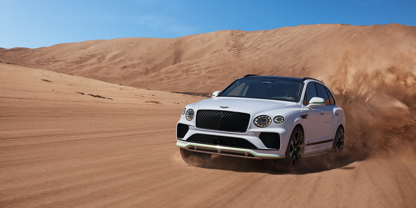 Bentley Hampshire Bentley Bentayga Speed SUV front three quarter in Snow Quarts Pearlescent by Mulliner white paint driving dynamically through the desert