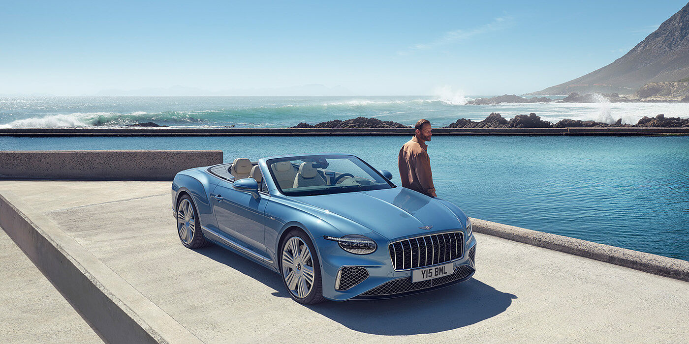 Bentley Hampshire New Bentley Continental GTC Azure convertible front view in Light Windsor blue paint with 22 inch ten spoke wheels parked by the sea in the sunshine