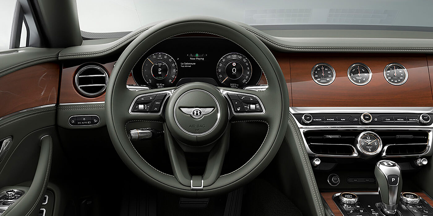 Bentley Hampshire New Bentley Flying Spur sedan front cabin in Cumbrian Green hide and Crown Cut walnut veneer showing steering wheel and Rotating Display with three clocks on face
