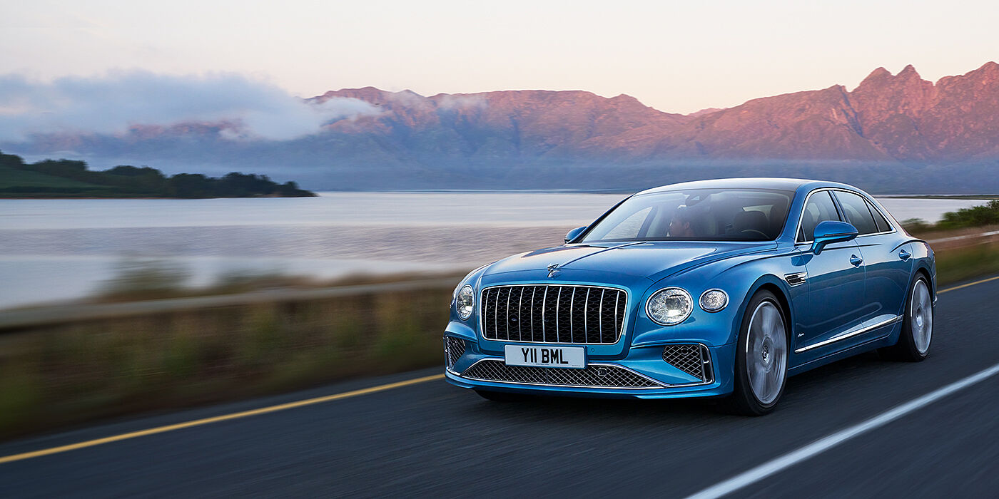 Bentley Hampshire New Bentley Flying Spur Azure sedan in Light windsor blue paint by Mulliner, with 22 inch Azure wheels and chrome straight vaned grille driving on a mountain road
