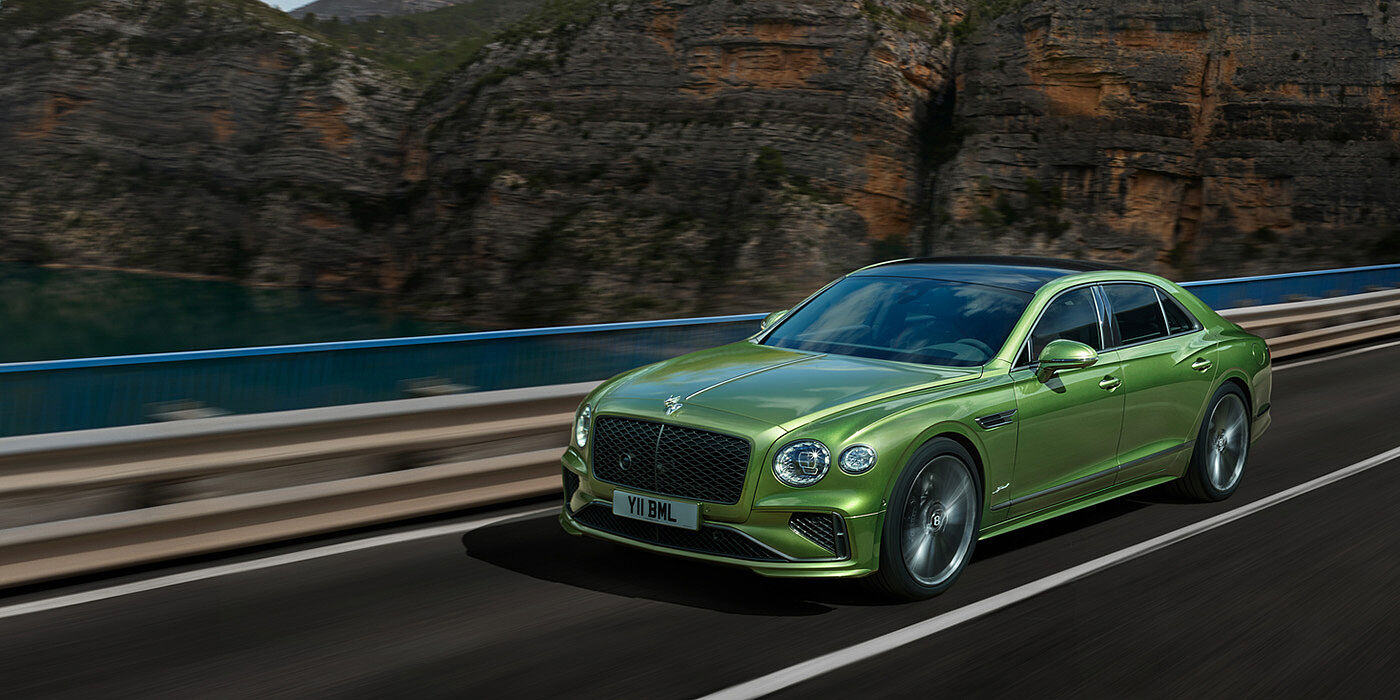 Bentley Hampshire Bentley New Flying Spur Speed v8 hybrid sedan driving dynamically on a mountain road in Tourmaline Green paint