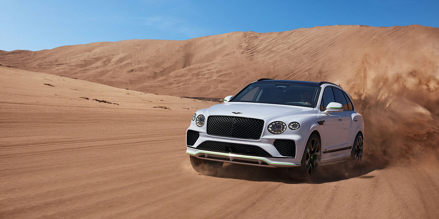 Bentley Hampshire Bentley Bentayga Speed SUV front three quarter in Snow Quarts Pearlescent by Mulliner white paint driving dynamically through the desert