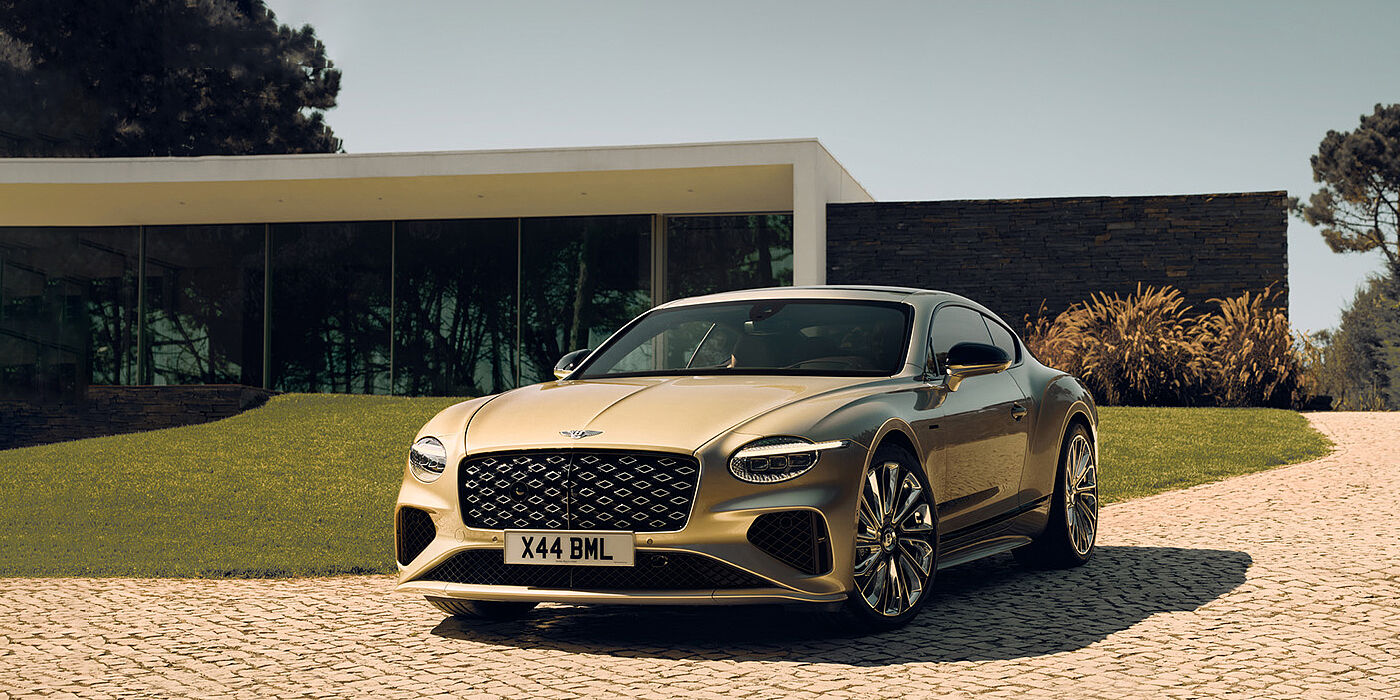 Bentley Hampshire Bentley Continental GT Mulliner coupe front three quarters in Patina paint parked outside a glass fronted building with a grass lawn behind it
