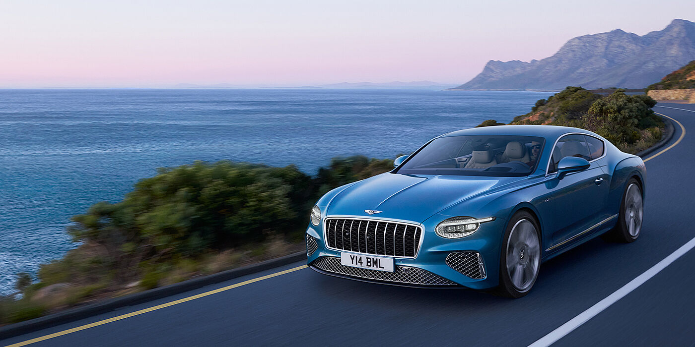 Bentley Hampshire New Bentley Continental GT Azure coupe in Light Windsor blue paint with 22 inch Azure wheels and chrome grill, driving dynamically by the sea