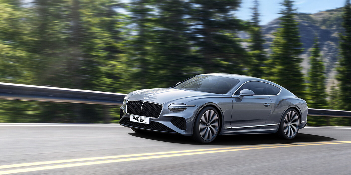 Bentley Hampshire New Bentley Continental GT coupe in Silverlake paint and 22 inch ten-spoke wheels, driving dynamically on a tree-lined road in the sunshine