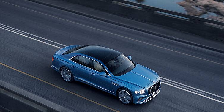 Bentley Hampshire New Bentley Flying Spur Azure sedan in Light windsor blue paint by Mulliner, with 22 inch Azure wheels seen from overhead driving dynamically on a country road