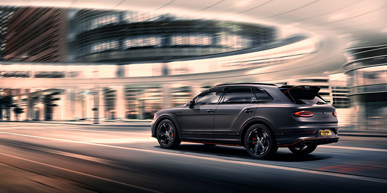 Bentley Hampshire Bentley Bentayga S Black Edition SUV rear three quarter in Anthracite Satin paint driving dynamically through a city at night
