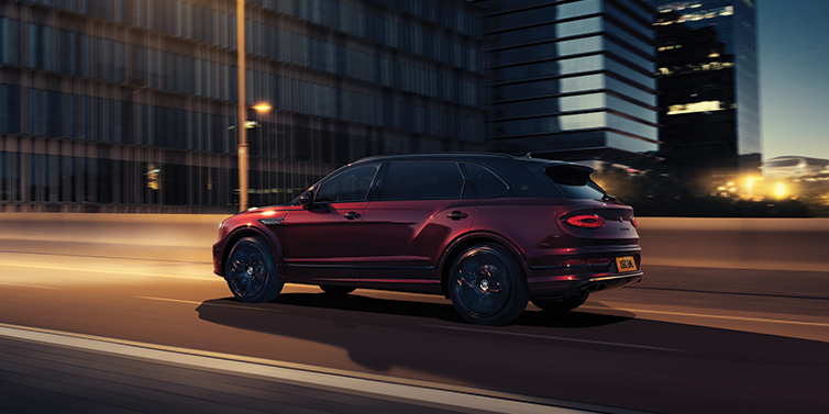 Bentley Hampshire Bentley Bentayga Extended Wheelbase Mulliner SUV in Cricket Ball red paint driving dynamically in city at night