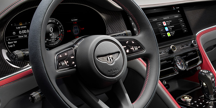 Bentley Hampshire Bentley Flying Spur Speed sedan front interior detail showing steering wheel and driver screens surrounded with Hotspur red and Gravity Grey hides